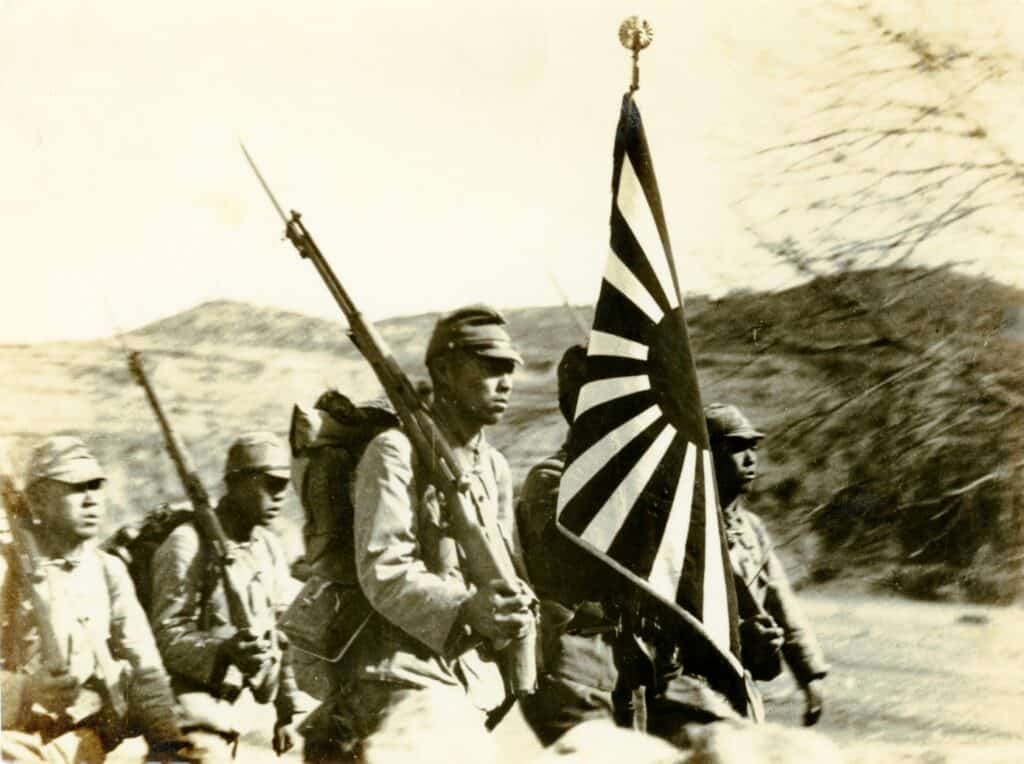 Black and white photo of Japanese soldiers carrying WWII era flag.