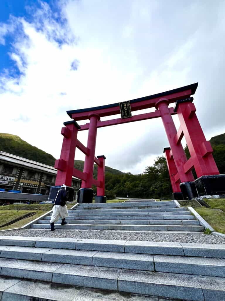 Large red torii gate with a man climbing the steps approaching it.