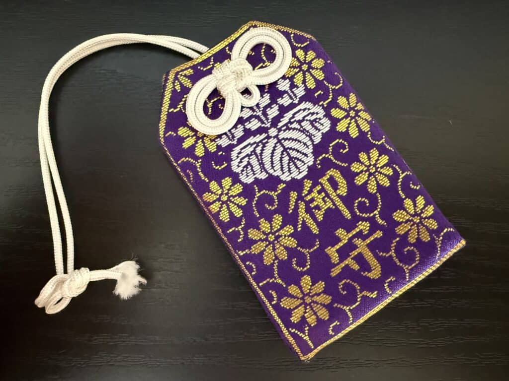 Purple and gold embroidered packet with string. Omamori charm.