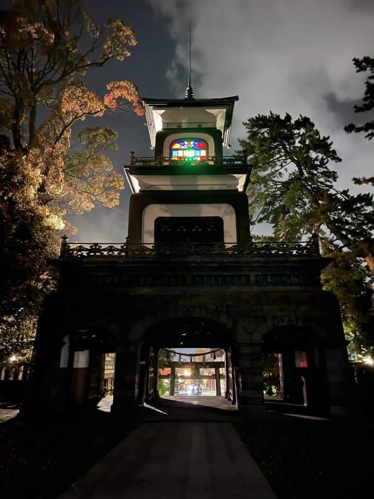 Three-story tower with stained glass windows at the top, emanating colored light in the darkness.