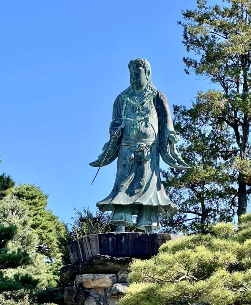 Statue of an ancient Japanese with drawn sword in hand, against the blue sky.